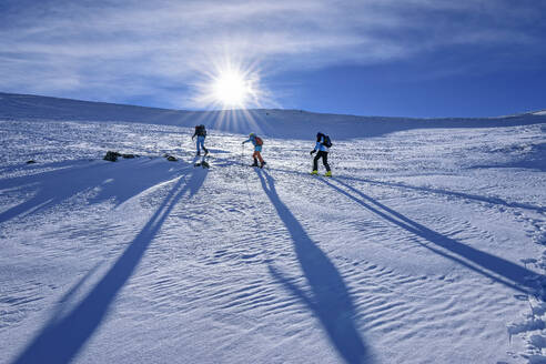 Österreich, Tirol, Die Sonne scheint über drei Skifahrern, die in den Kitzbüheler Alpen durch den Schnee fahren - ANSF00264