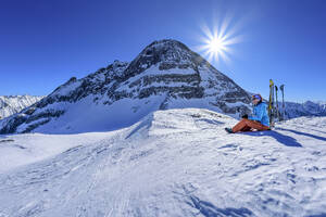 Österreich, Tirol, Die Sonne scheint über einer Skifahrerin, die am Torhelm eine Pause einlegt - ANSF00268