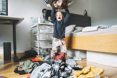 Carefree boy throwing laundry clothes in bedroom at home - NDEF00614