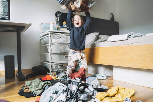 Unbekümmerter Junge wirft Wäsche im Schlafzimmer zu Hause - NDEF00614