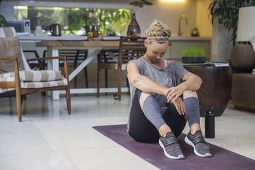 Frau in Sportkleidung übt Yoga auf einer Übungsmatte zu Hause - IKF00537