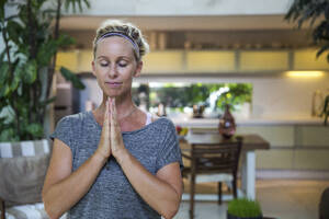 Frau mit gefalteten Händen beim Meditieren zu Hause - IKF00539