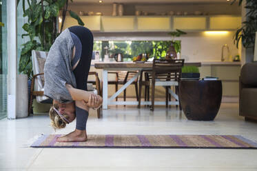 Woman practicing Big Toe Pose in living room at home - IKF00545