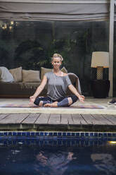 Woman meditating near swimming pool at home - IKF00549