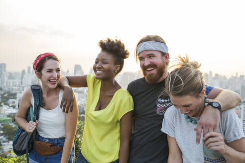 Friends laughing together with city in background at sunset - IKF00588