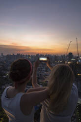 Friends photographing city with sky at dusk - IKF00605