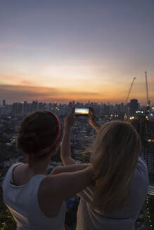 Freunde fotografieren Stadt mit Himmel in der Abenddämmerung - IKF00605