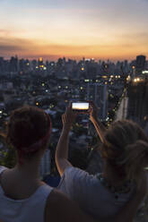 Friends photographing cityscape at dusk through smart phone - IKF00606