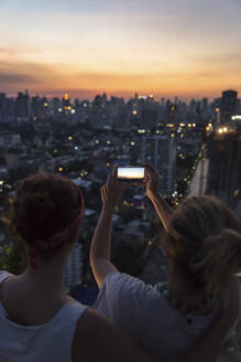 Freunde fotografieren Stadtbild in der Abenddämmerung mit dem Smartphone - IKF00606
