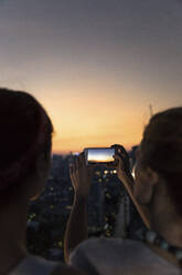 Freunde fotografieren Stadt mit orangefarbenem Himmel in der Abenddämmerung durch Smartphone - IKF00607