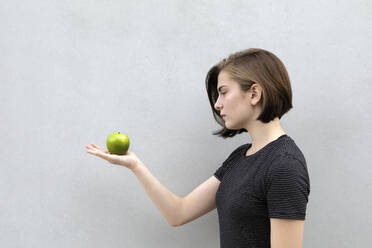Teenager-Mädchen hält grünen Apfel vor grauem Hintergrund - PSTF01054