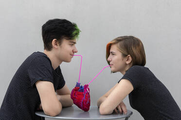Teenager-Paar trinkt aus Modell Herz vor grauem Hintergrund - PSTF01061