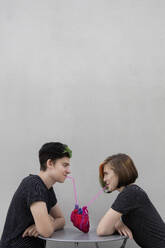 Teenager-Paar trinkt aus Herz gegen grauen Hintergrund - PSTF01062