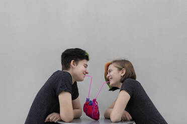 Fröhliches Teenager-Paar trinkt aus dem Herzen vor grauem Hintergrund - PSTF01063