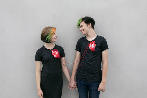 Teenage couple connected with hearts and holding hands against gray background - PSTF01075