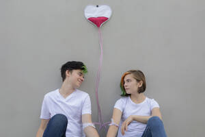 Teenage couple connected with IV drips in front of gray wall - PSTF01088