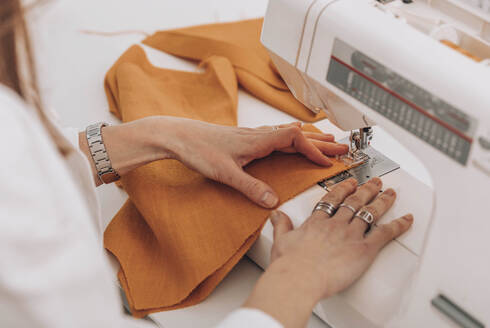 Seamstress sewing fabric through machine at workshop - ADF00019