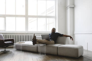 Businessman working with laptop on sofa at home - EYAF02608