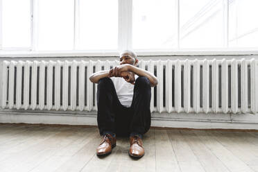 Thoughtful man sitting on hardwood floor near heater at home - EYAF02627