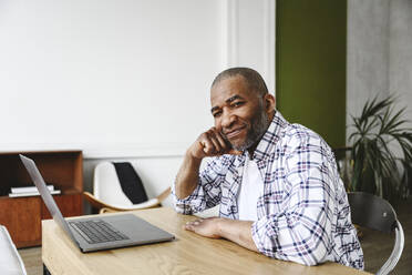 Geschäftsmann lehnt sich mit seinem Laptop im Büro zu Hause an einen Tisch - EYAF02632