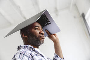 Gelangweilter Geschäftsmann trägt Laptop auf dem Kopf - EYAF02634