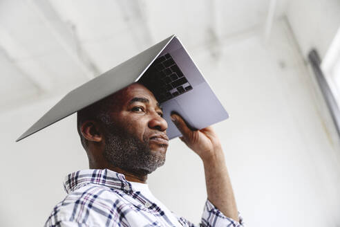 Bored businessman carrying laptop on head - EYAF02634