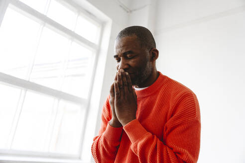 Mature man praying with hands clasped at home - EYAF02646