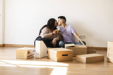 Couple kissing sitting by cardboard boxes in new home - JCCMF10326