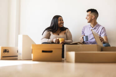 Smiling couple with coffee cup sitting by cardboard boxes in new home - JCCMF10327
