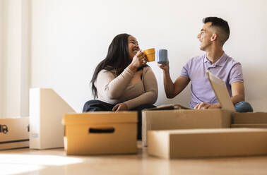 Lächelndes Paar genießt Kaffee neben Kartons in der neuen Wohnung - JCCMF10328