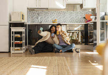 Ein fröhliches Paar hält einen Moment mit einer Kaffeetasse in der Hand fest, während es ein Selfie in seiner Küche macht - JCCMF10332
