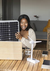 Lächelnde Geschäftsfrau mit Sonnenkollektor, die über einen Laptop ein Videogespräch führt - JCCMF10337