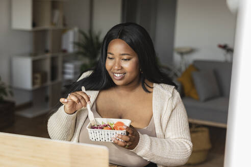 Freiberufliche Frau isst Salat vor dem Laptop im Heimbüro - JCCMF10339