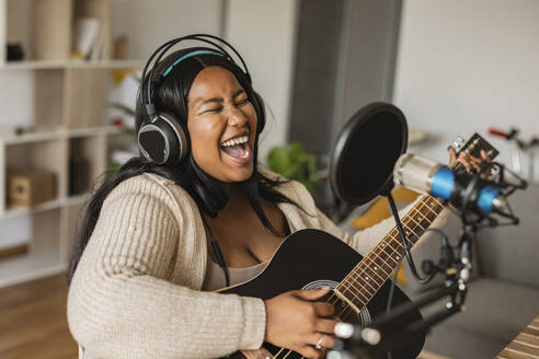 Woman singing and playing guitar on microphone at home - JCCMF10351