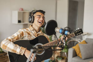 Happy man singing and playing guitar at home - JCCMF10354