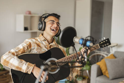Happy man singing and playing guitar at home - JCCMF10354
