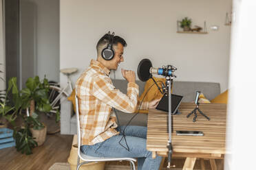 Man podcasting in front of smart phone and tablet PC sitting at home - JCCMF10357