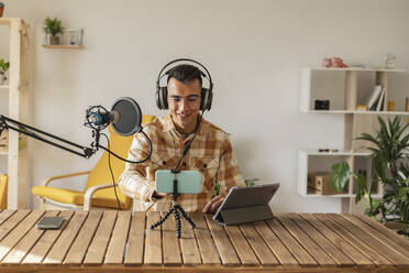 Man podcasting in front of smart phone and tablet PC at desk - JCCMF10358