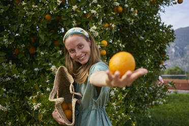 Glückliche Frau mit Orange in der Hand im Obstgarten - ANNF00151