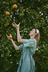 Frau jongliert mit Orangen vor einem Baum im Obstgarten - ANNF00172