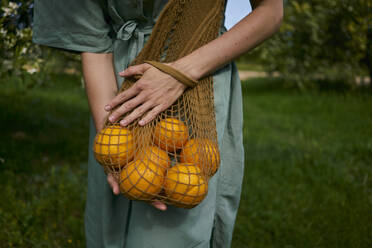 Frau hält wiederverwendbare Tasche mit Bio-Orangen im Obstgarten - ANNF00176