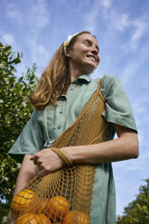 Contemplative woman with oranges in mesh bag at orchard - ANNF00177