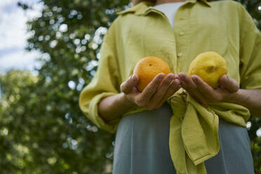 Woman holding citrus fruits standing in orchard - ANNF00206