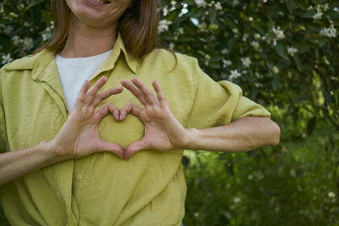Woman making heart gesture on breast in garden - ANNF00209