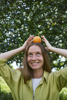 Frau balanciert Orange auf dem Kopf im Garten - ANNF00212