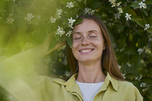 Lächelnde Frau mit geschlossenen Augen an einer Orangenblüte im Garten - ANNF00226