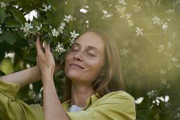 Frau mit geschlossenen Augen in der Nähe von Orangenblüten im Garten - ANNF00227