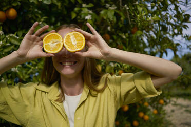 Woman covering eyes with orange slices at orchard - ANNF00237
