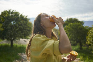 Frau isst frische saftige Orangen im Obstgarten - ANNF00239