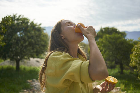 Woman eating fresh juicy orange in orchard - ANNF00239